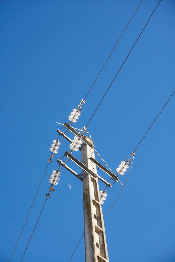 About Us ! A towering utility pole with cables and insulators against a bright, clear blue sky.